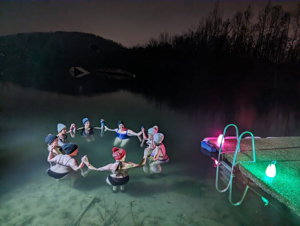 Eisbadegruppe steht nachts gemeinsam im Kreis im See