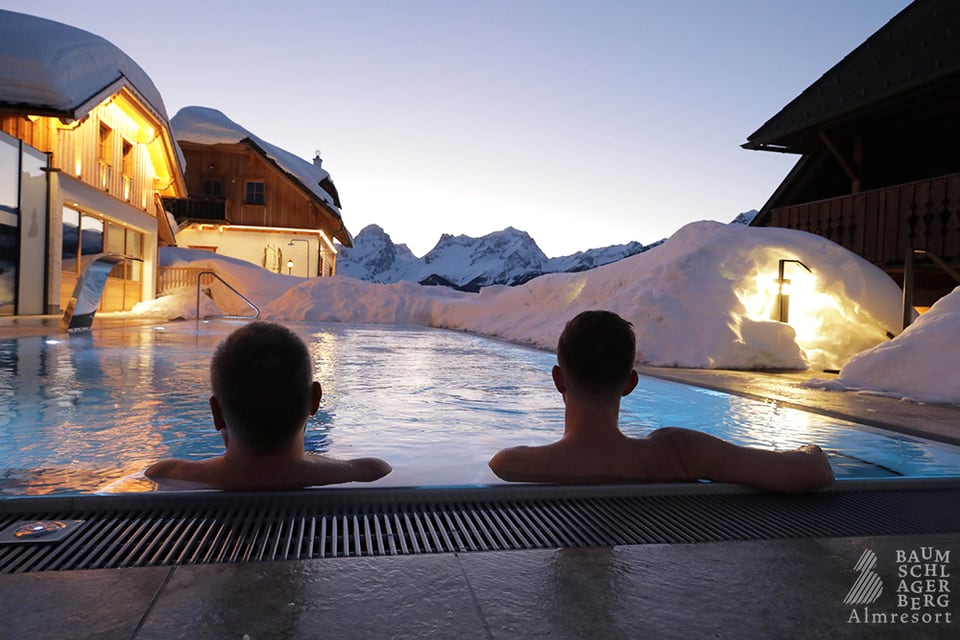 Zwei Gäste im beheizten Außenpool des verschneiten Bergchalets in Vorderstoder